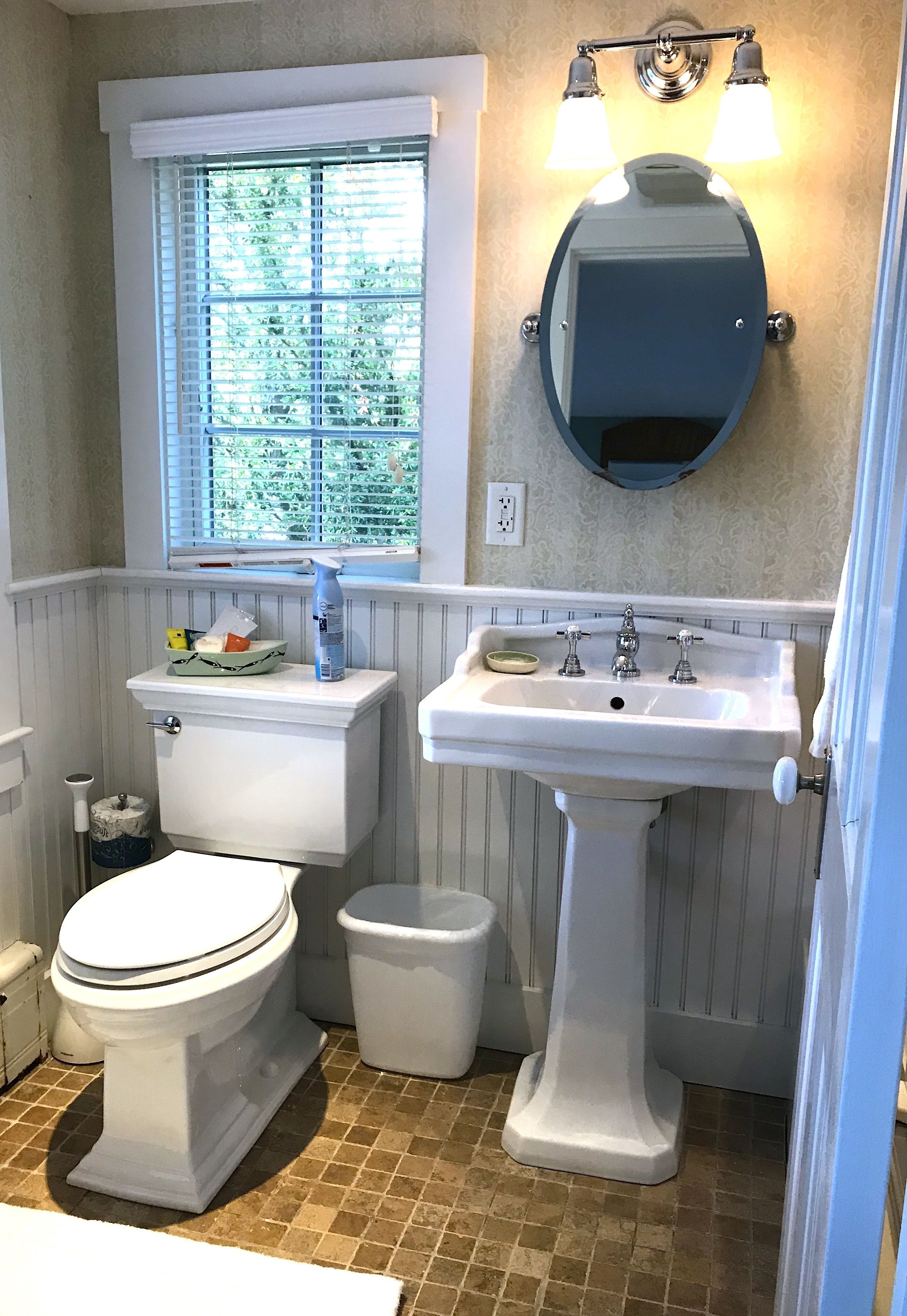 A bathroom with a toilet, bidet, sink, and window with blinds.