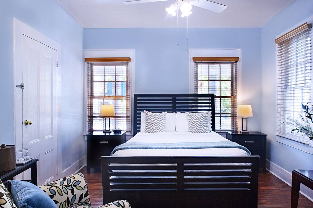 A bedroom with a bed, two bedside tables, a nightstand, a ceiling fan, and windows with blinds.