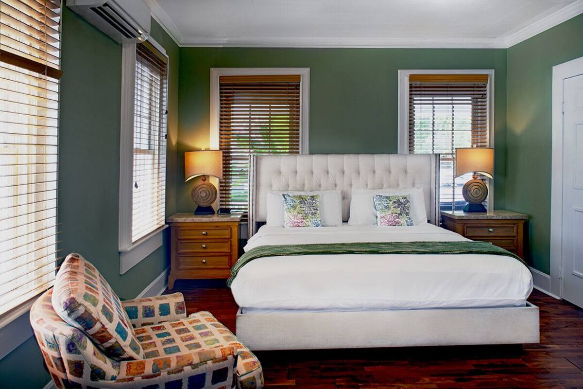 A bedroom with a large bed, two bedside tables with lamps, a chair, and a window with blinds.