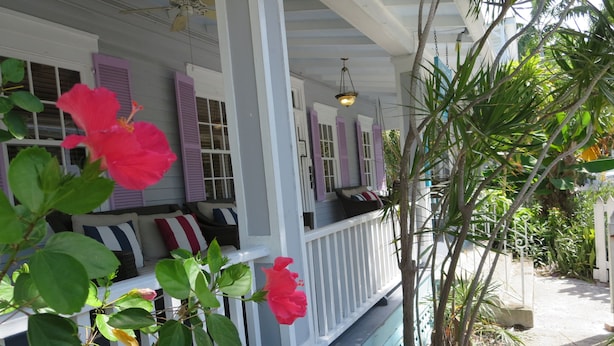 A covered porch with a white railing, purple shutters, and a seating area with cushions. - The Inn on Fleming (Key West)