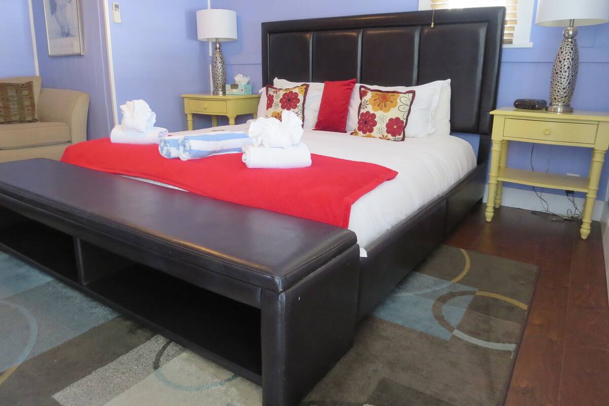 A neatly made bed with a red blanket and pillows, a bedside table with a lamp, and a small nightstand with a lamp.