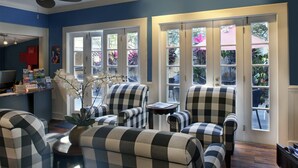 A living room with checkered armchairs, a small table, and a ceiling fan. Large windows with glass doors lead to a garden. - The Inn on Fleming (Key West)