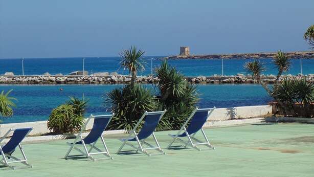 A pool area with lounge chairs and a view of the sea and a rocky outcrop. - Palm Beach Hotel (Cinisi)