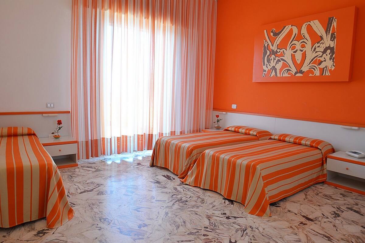 A hotel room with two beds, a large window with curtains, a painting on the wall, and a marble floor.