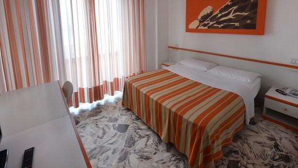 Ein Hotelzimmer mit Bett, Schreibtisch, Telefon und einem Gemälde an der Wand.