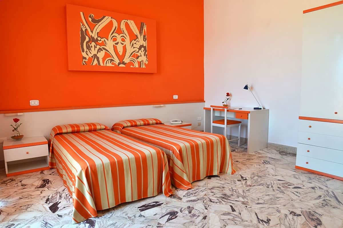 A room with two beds, a desk, a chair, a dresser, and a painting on the wall.