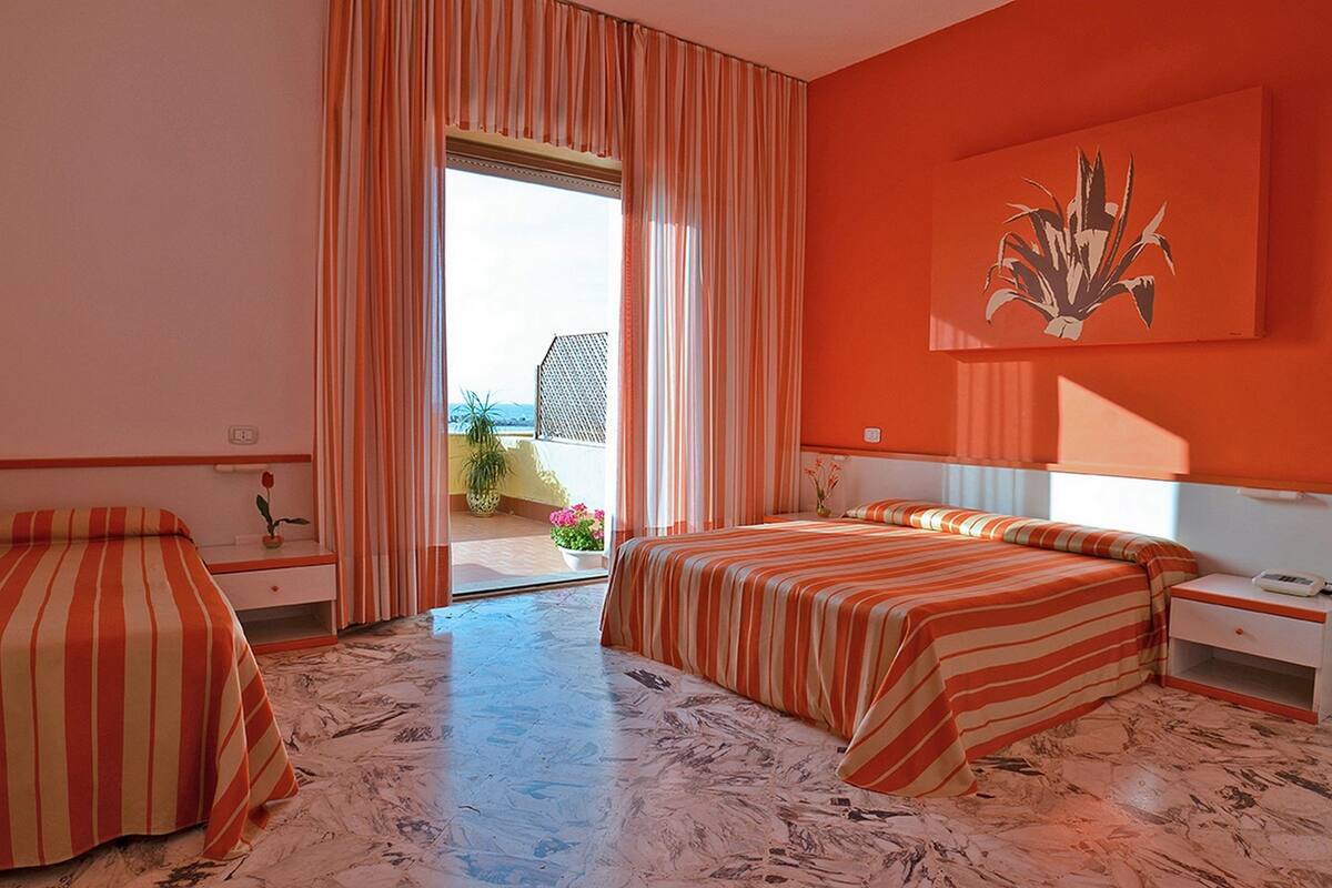 A hotel room with two beds, a large window with curtains, a painting on the wall, and a view of the outdoors.