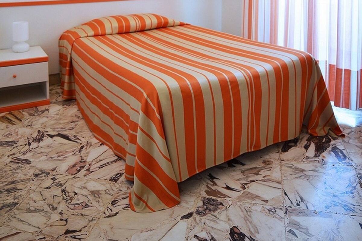 A hotel room with a bed, a nightstand, a lamp, a painting, and striped curtains.