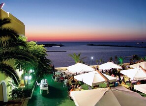 A beachside restaurant with outdoor seating, palm trees, and a view of the ocean at sunset. - Palm Beach Hotel (Cinisi)