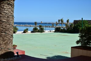 A courtyard with a pool, palm trees, and a view of the sea and a historic tower. - Palm Beach Hotel (Cinisi)