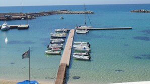 A marina with various boats docked, a pier extending into the water, and a rocky breakwater in the background. - Palm Beach Hotel (Cinisi)