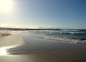 A beach with waves, a clear sky, and a distant shoreline with structures. - Palm Beach Hotel (Cinisi)