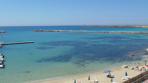 A beach with clear blue water, a rocky breakwater, and several beach umbrellas. - Palm Beach Hotel (Cinisi)