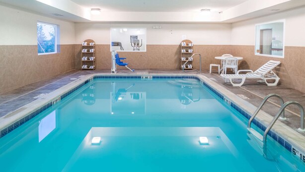A swimming pool with a blue tiled edge, a blue chair, a white lounge chair, and a shelf with towels. - Super 8 by Wyndham St Robert Ft Leonard Wood Area (St. Robert)