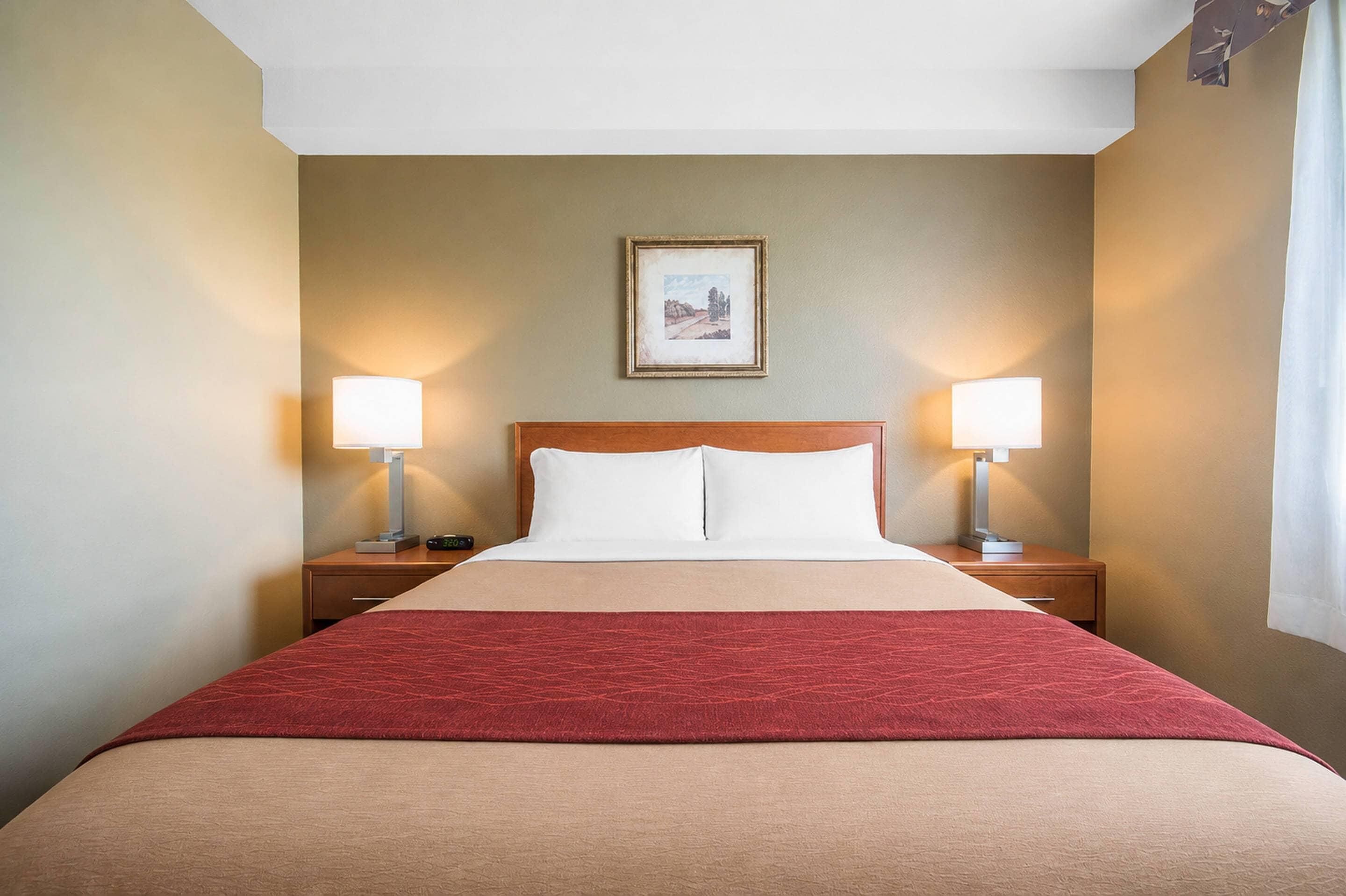 Een hotelkamer met een bed, twee nachtkastjes, een raam met gordijnen en een lijst met een afbeelding aan de muur.
