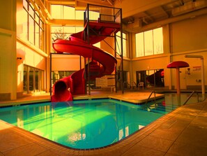 An indoor swimming pool with a red spiral slide, a lifeguard stand, and a view of the outside through large windows. - Comfort Inn & Suites Langley - Fraser Highway (Langley)