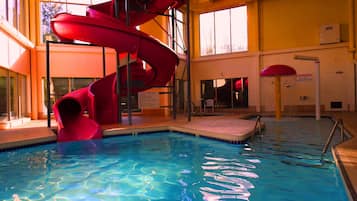 Una piscina con un tobogán espiral rojo, agua azul cristalina y un letrero que indica 'No hay salvavidas de servicio'.
