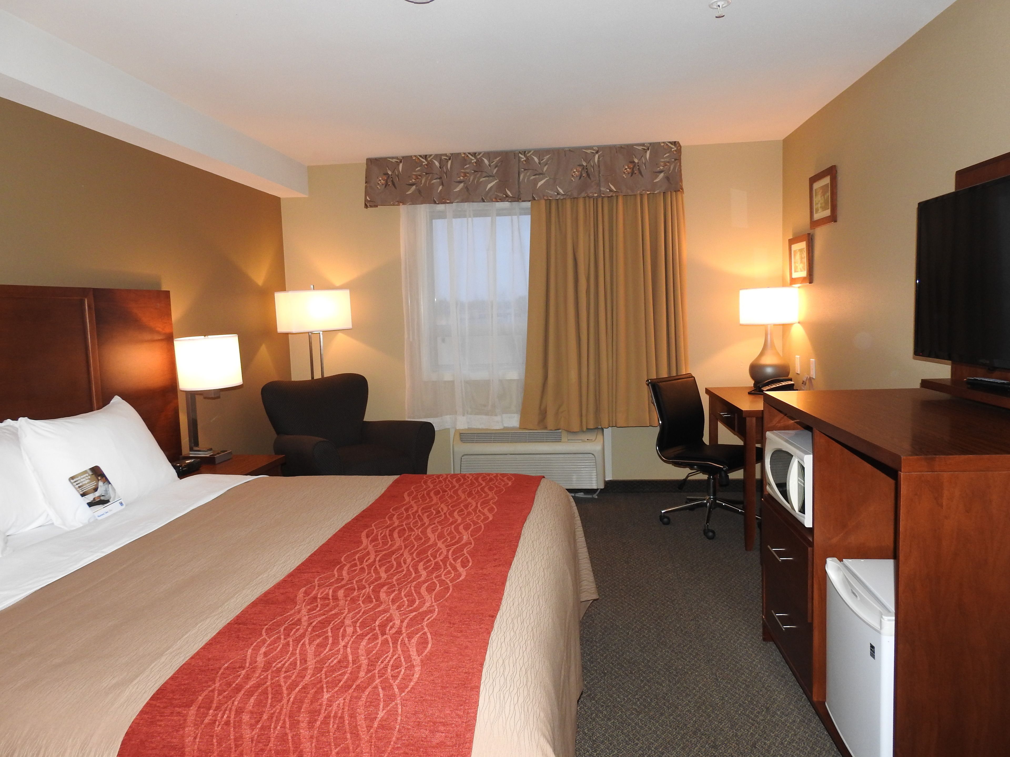 A hotel room with a bed, two chairs, a desk, a television, and a minibar.