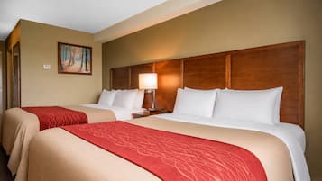 A hotel room with two beds, each with a red and beige bedspread, a wooden headboard, a nightstand with a lamp, and a painting on the wall.