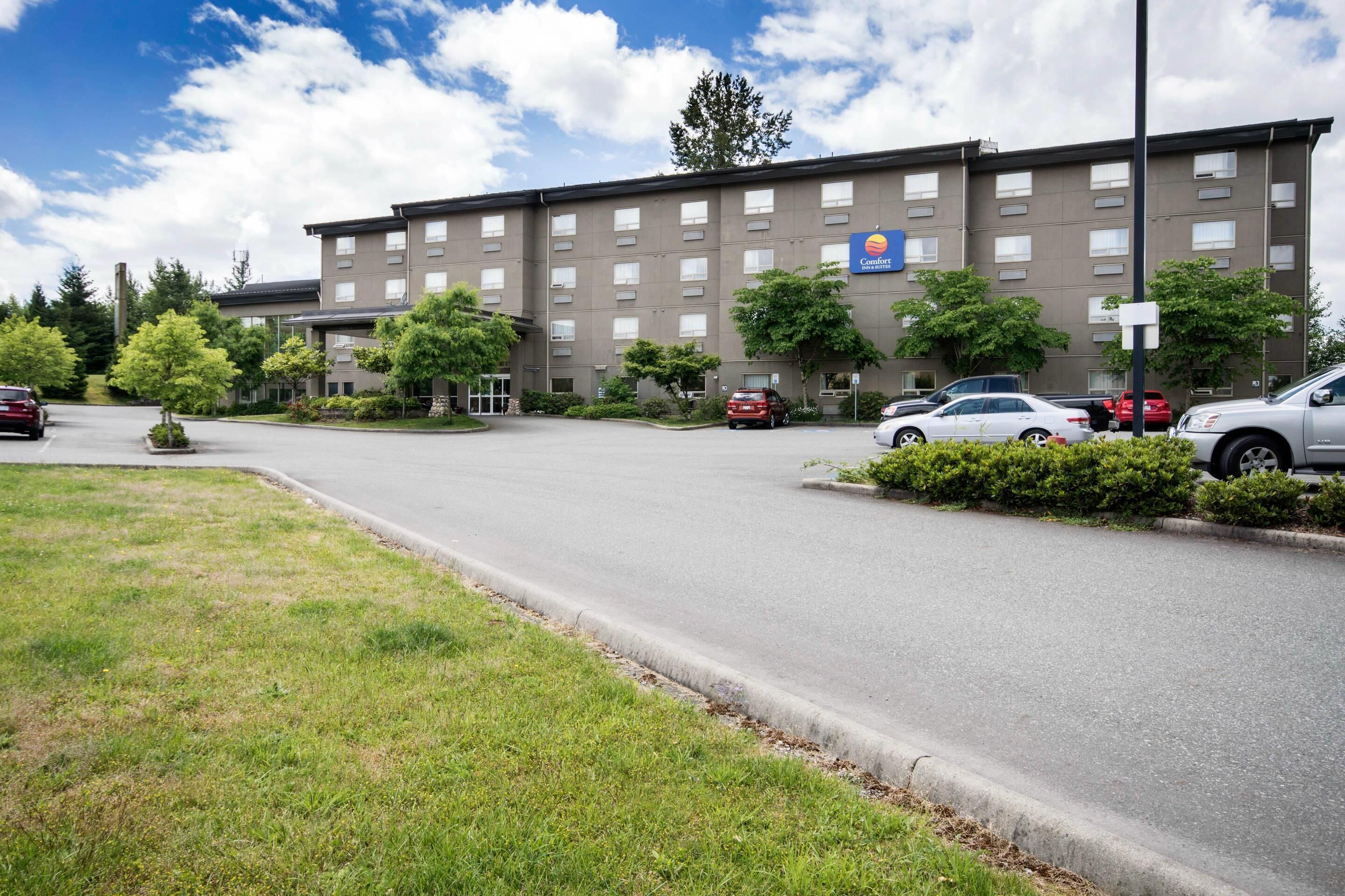 A multi-story hotel with a parking lot, trees, and a clear sky.