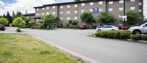 Un hotel de varios pisos con estacionamiento, árboles y cielo despejado.