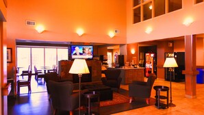 Eine Lobby mit Fernsehgerät, das eine Nachrichtensendung zeigt, Sitzbereichen und einer Coca-Cola-Getränkeautomaten.
