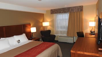 A hotel room with a bed, two bedside lamps, a chair, a desk with a computer, and a television.