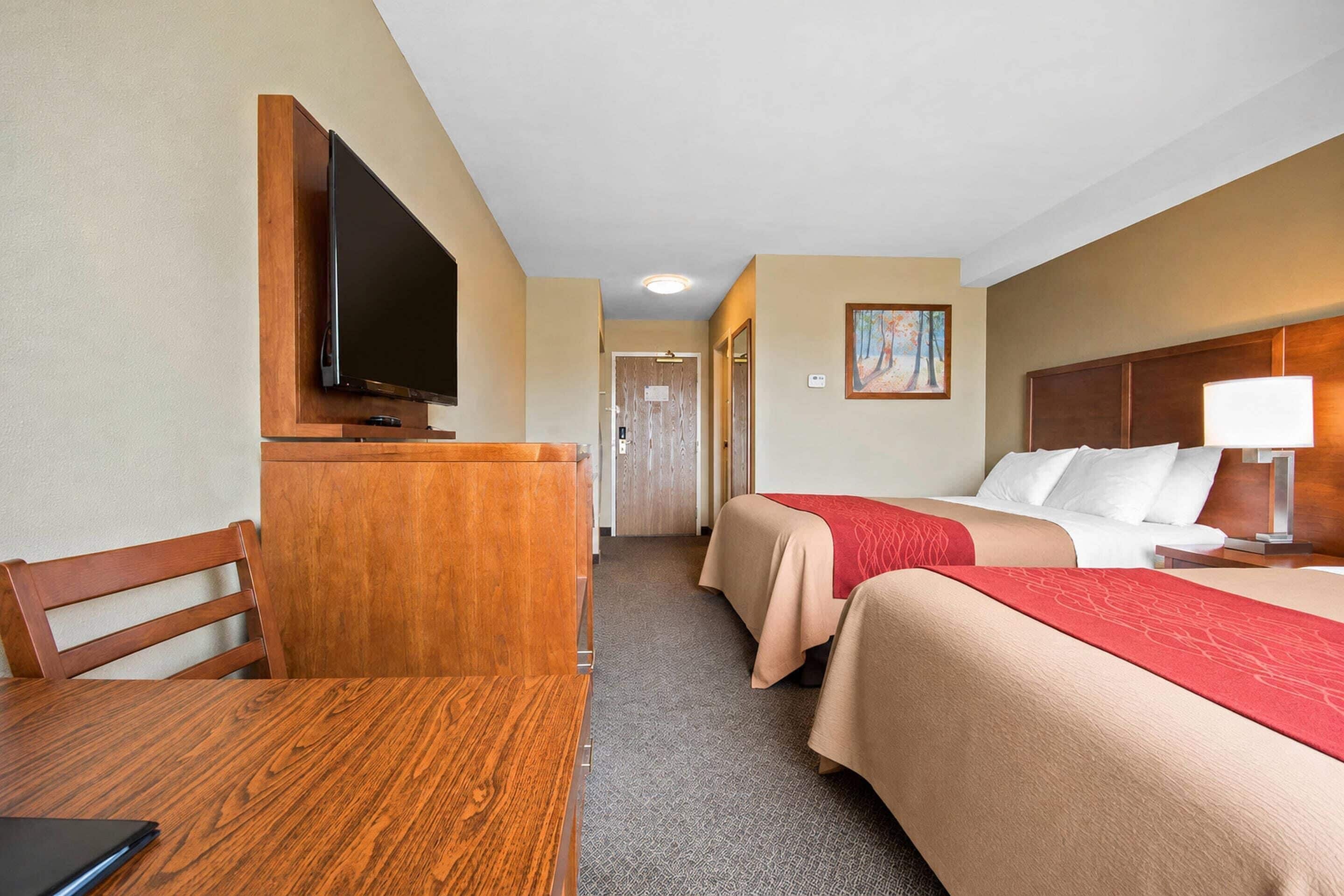 Habitación de hotel con escritorio, dos camas, televisor y un cuadro en la pared.