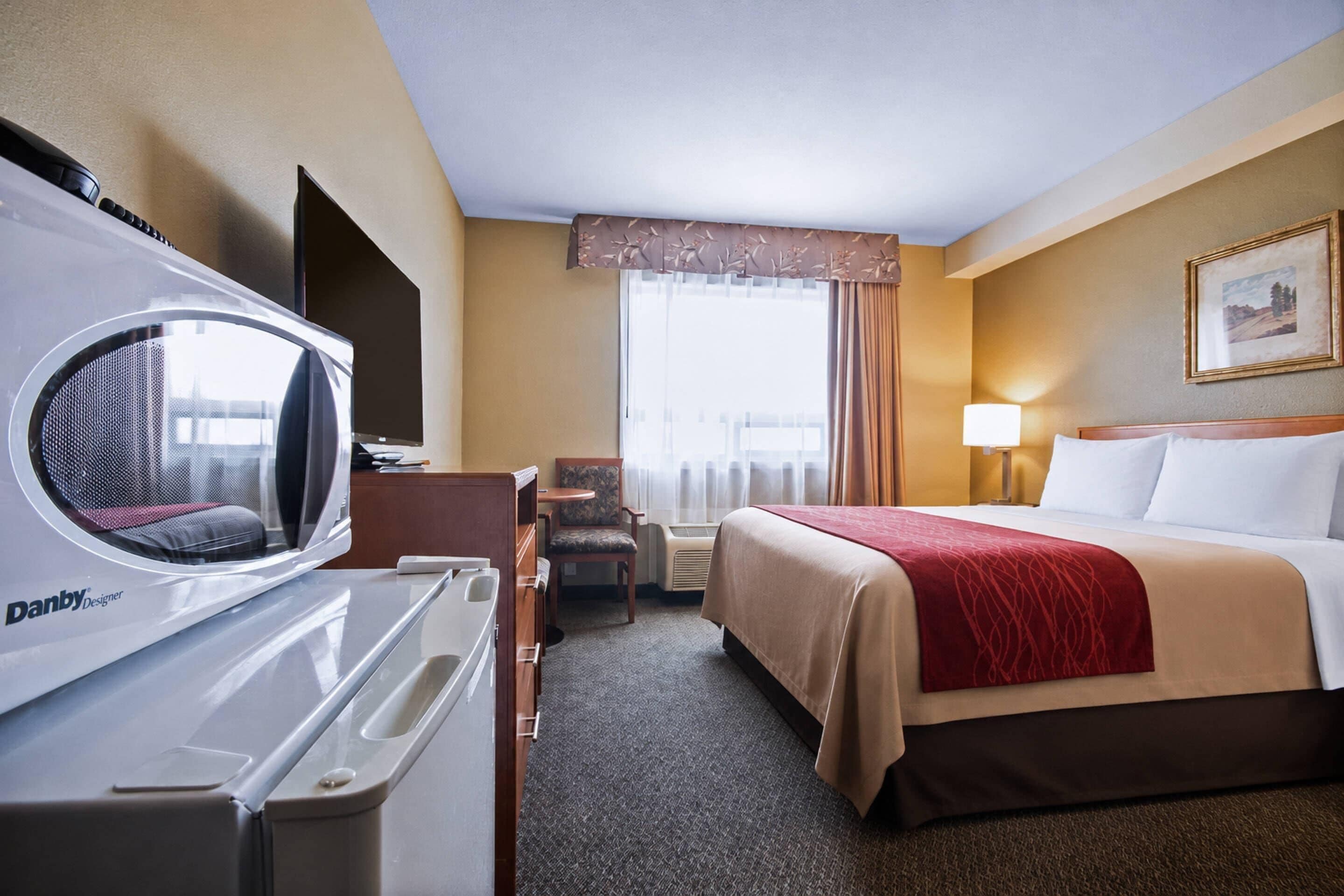 A hotel room with a bed, a desk, a chair, a heater, and a window with curtains.