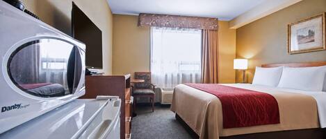 A hotel room with a bed, a desk, a chair, a heater, and a window with curtains.