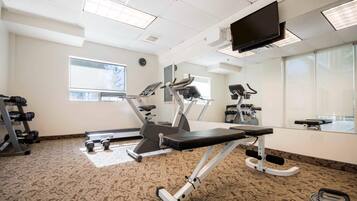 A gym with cardio machines, weight stations, and a TV screen.