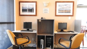 Ein Arbeitsplatz mit zwei Schreibtischen, jeweils ausgestattet mit einem Computer und einem Stuhl. An der Wand befinden sich gerahmte Bilder und ein Schild für Kopierservice.