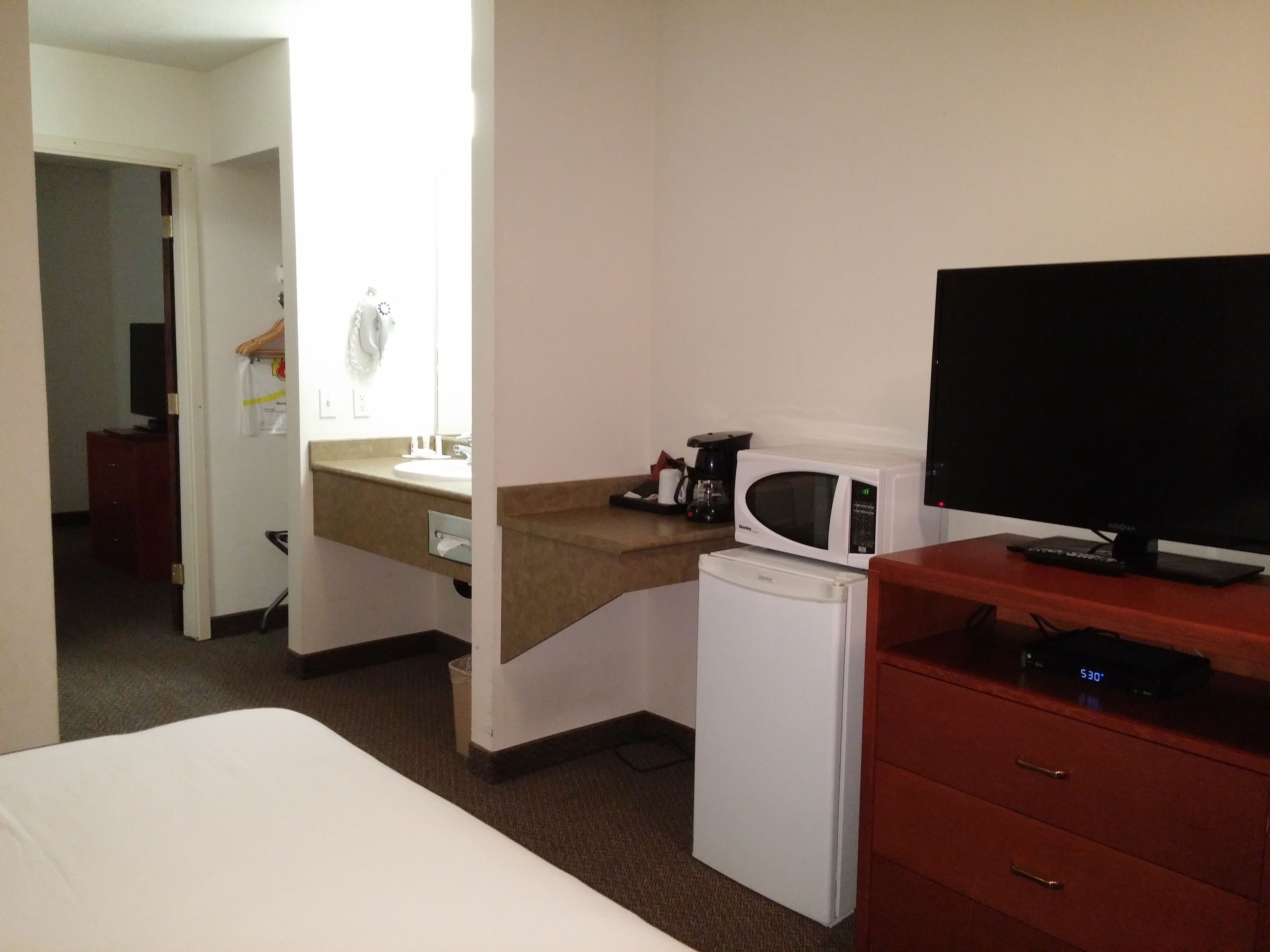 Una habitación de hotel con una cama, un escritorio con computadora, un microondas, una cafetera y un televisor.