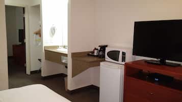 Una habitación de hotel con una cama, un escritorio con computadora, un microondas, una cafetera y un televisor.