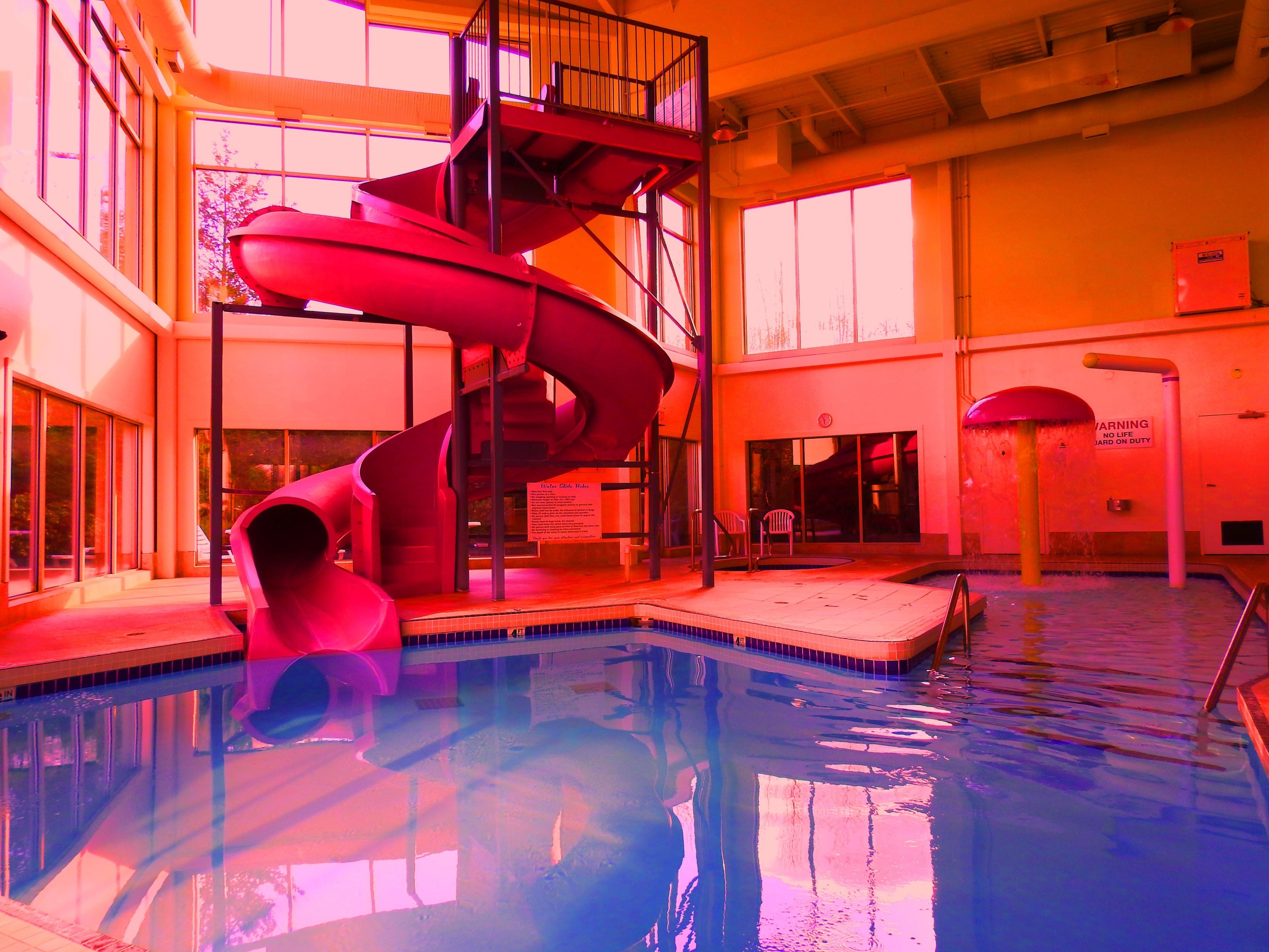 A swimming pool with a red spiral slide, indoor seating area, and large windows.