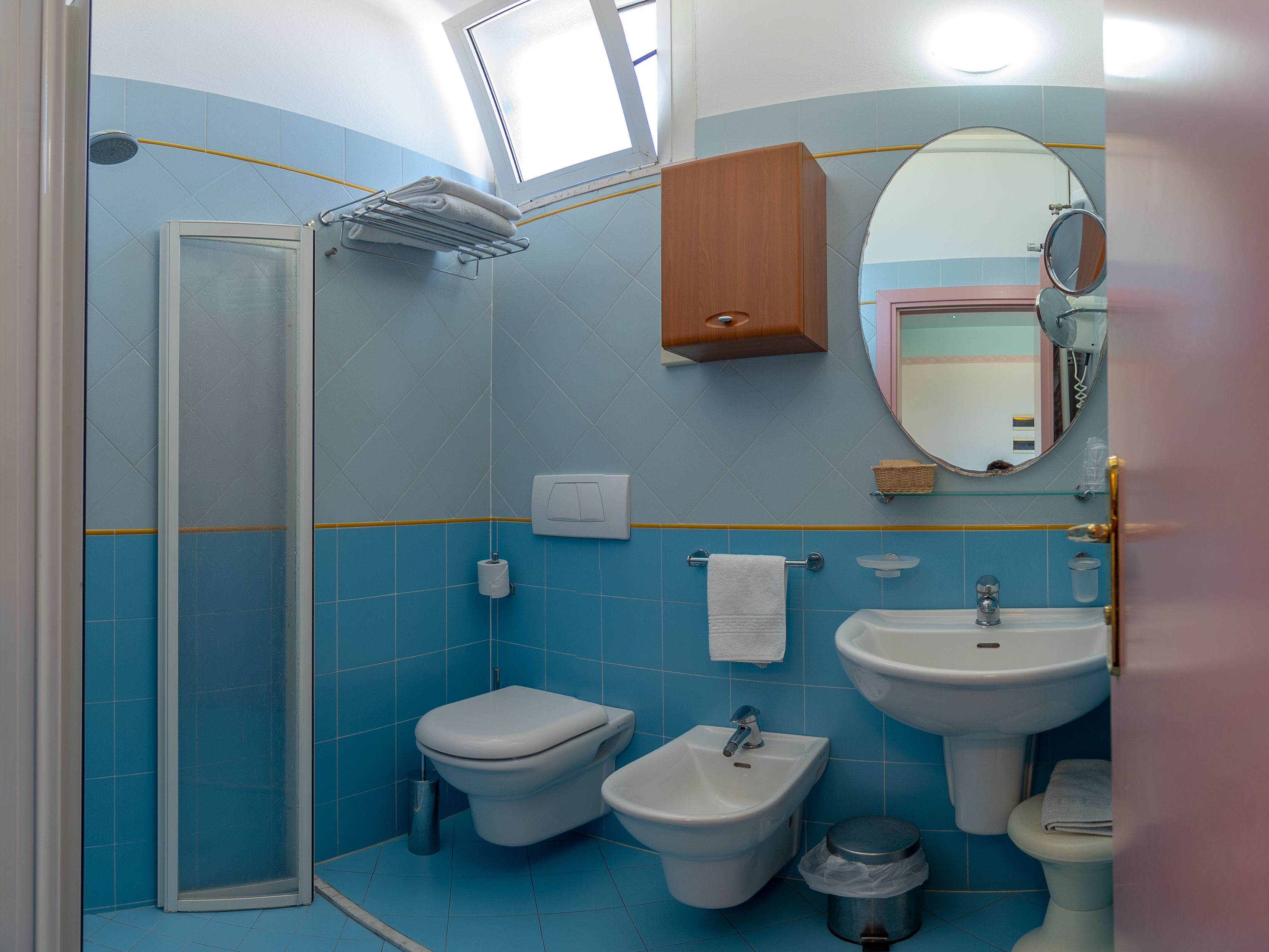A bathroom with a shower, toilet, bidet, sink, and a mirror.