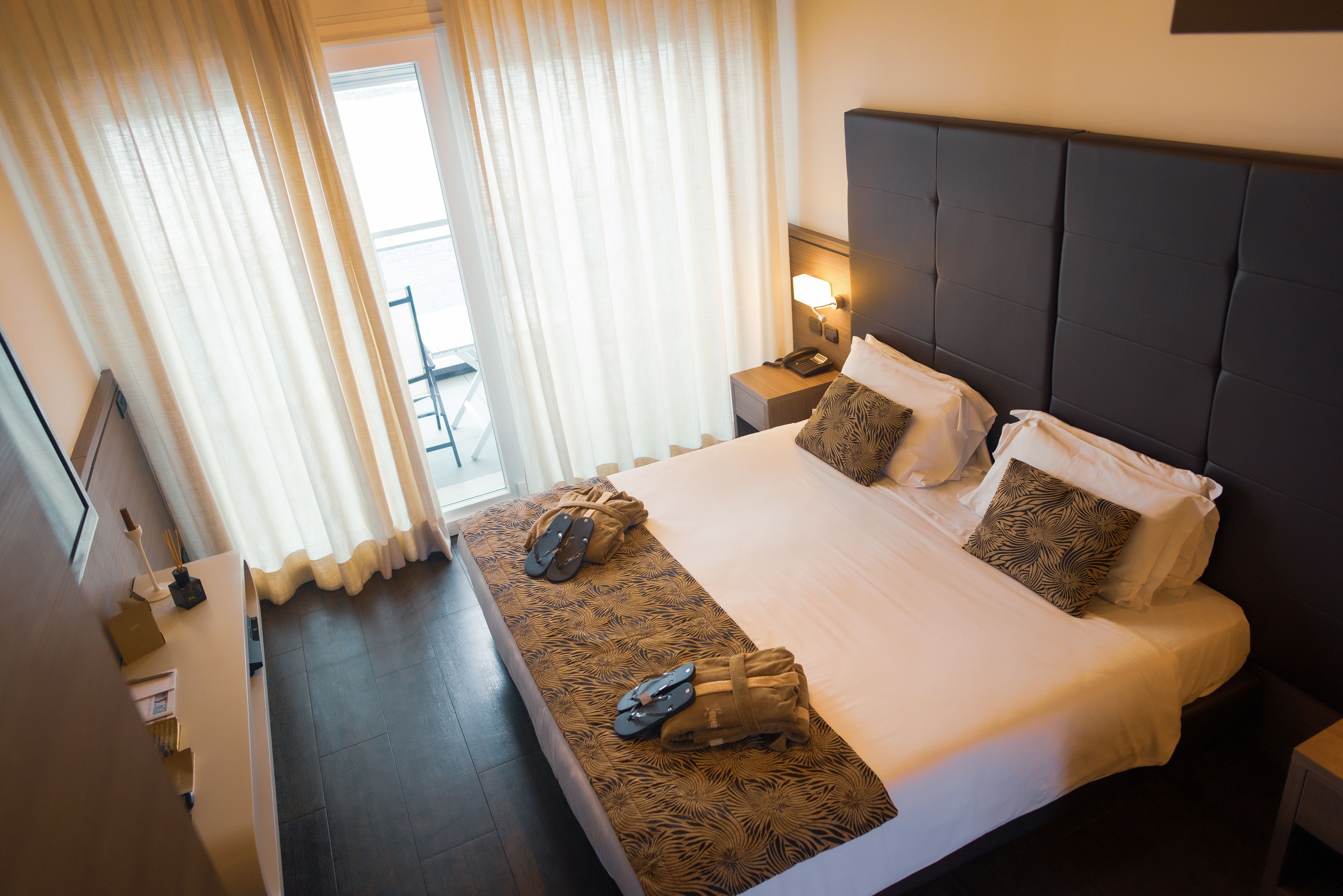 A hotel room with a large bed, a nightstand with a lamp, and a window with curtains.