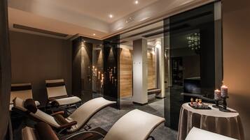 Un moderno spa con sillones reclinables, un separador de vidrio y una mesa con velas.