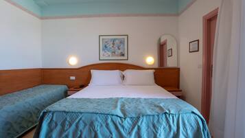 A hotel room with a single bed, a bedside table, a lamp, a wall-mounted picture, and a door.