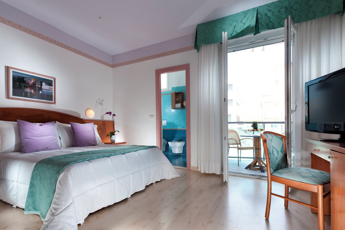 Een hotelkamer met een bed, een televisie, een stoel en uitzicht op buiten.