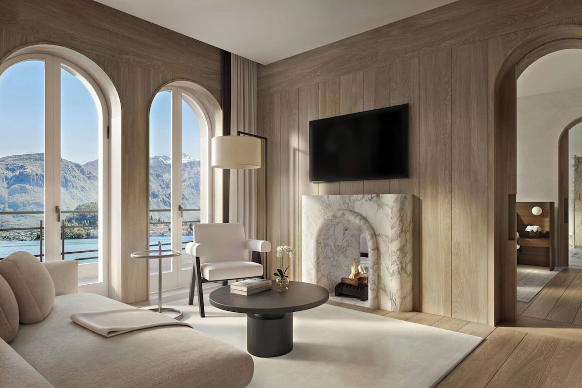 A modern living room with a fireplace, a flat-screen TV mounted on the wall, and a view of mountains through large windows.