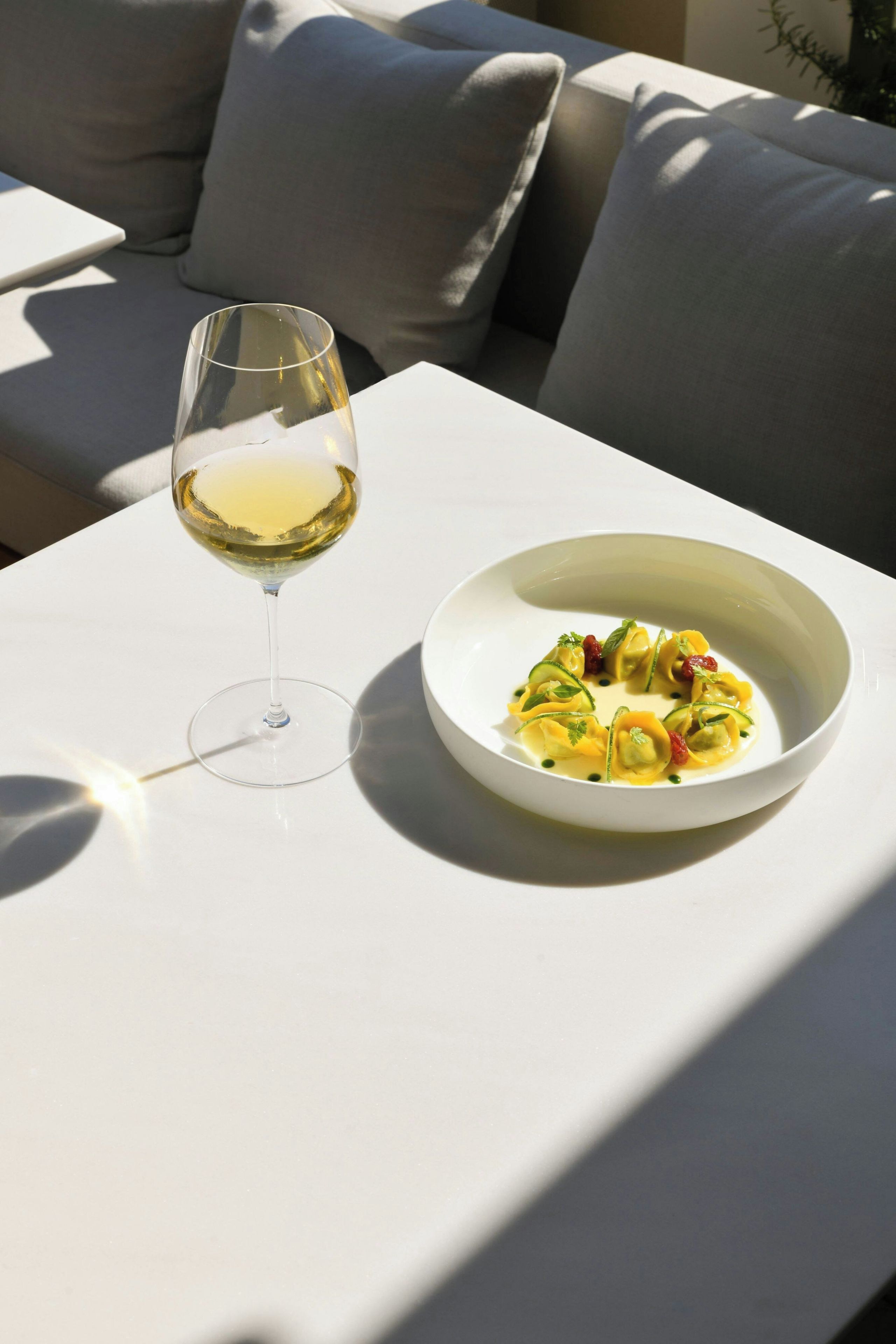 Een witte tafel met een glas witte wijn en een schaal eten.
