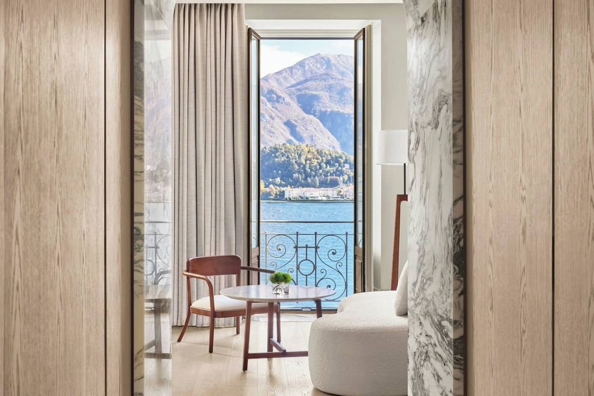 A modern interior with a marble archway leading to a balcony with a view of a lake and mountains.
