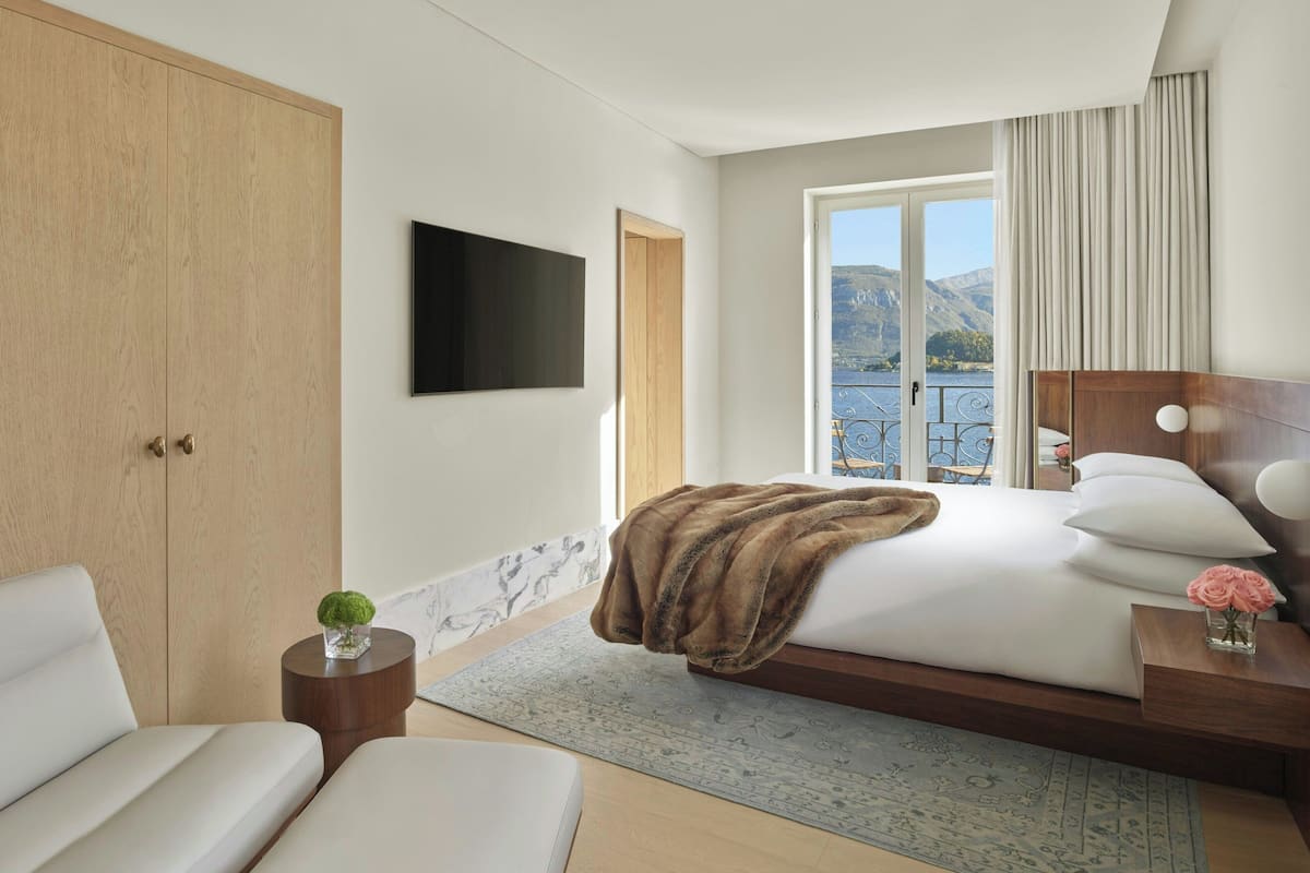 A modern hotel room with a large bed, a seating area, a TV, and a balcony with a mountain view.