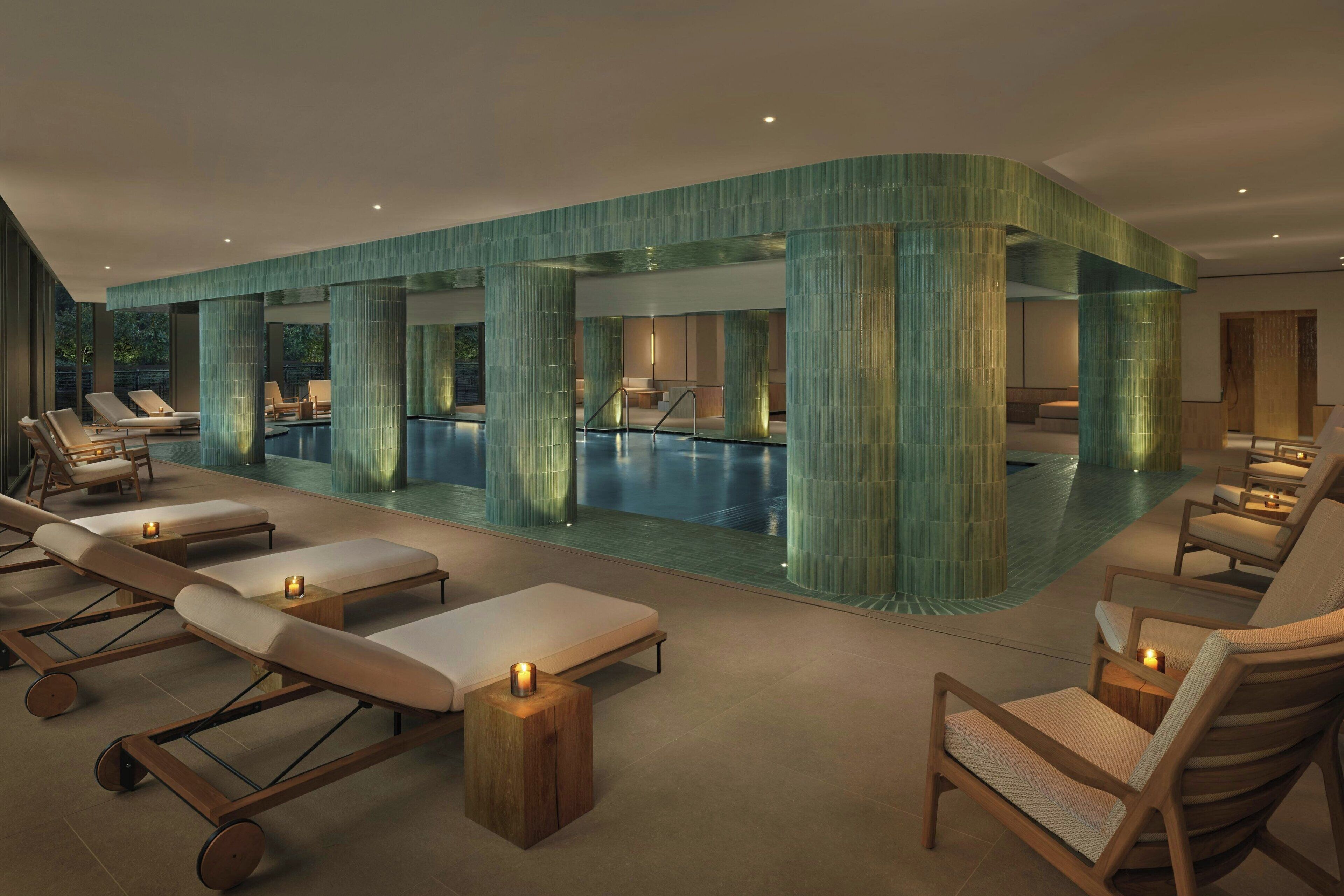Un área interior de piscina moderna con sillones de descanso y una piscina central, rodeada de columnas grandes y texturizadas.