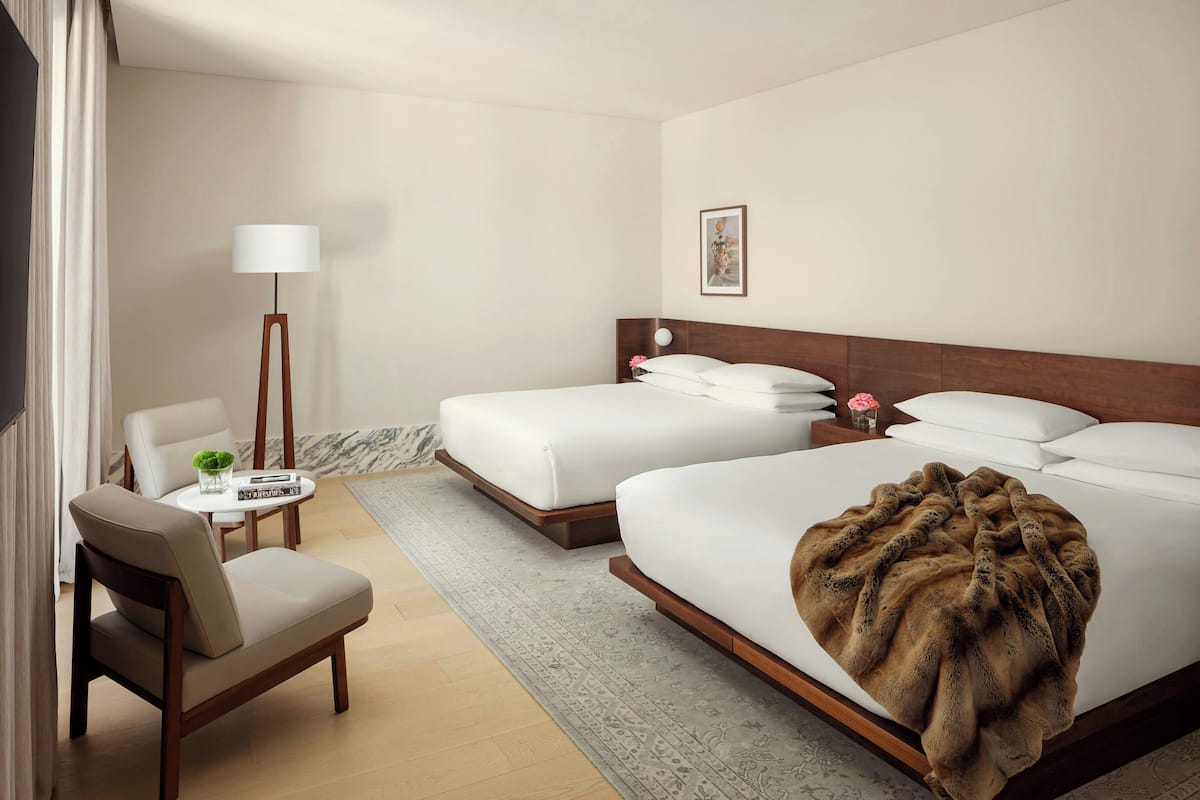 A hotel room with a bed, a chair, a small table with a lamp, and a picture on the wall.