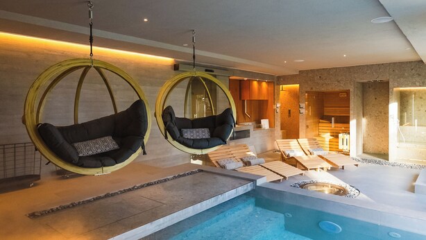 Een modern binnenzwembad met twee hangstoelen, loungestoelen en een jacuzzi.