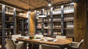 Een restaurant met een houten tafel en stoelen, omringd door flessen op planken.