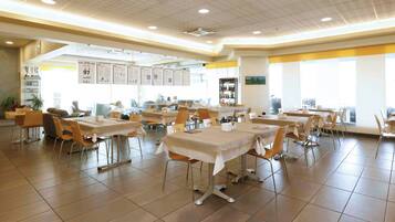 A spacious dining area with multiple tables and chairs, a ceiling with recessed lighting, and a view of the outdoors through large windows.
