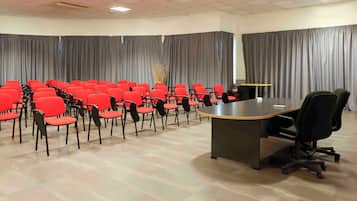 Una sala de conferencias con una larga mesa, sillas rojas y cortinas grises.
